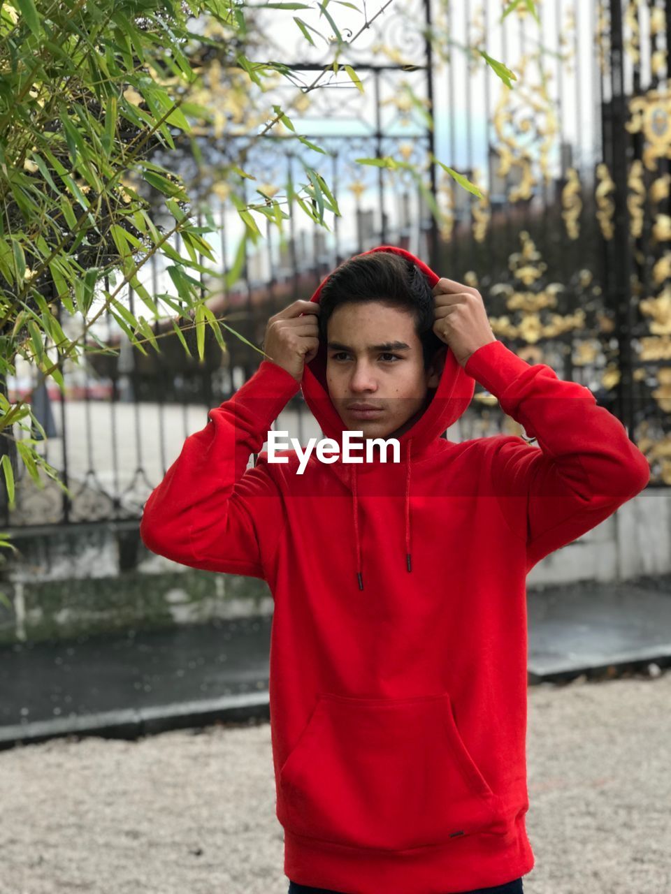 Thoughtful young man wearing red hooded shirt while standing against built structure