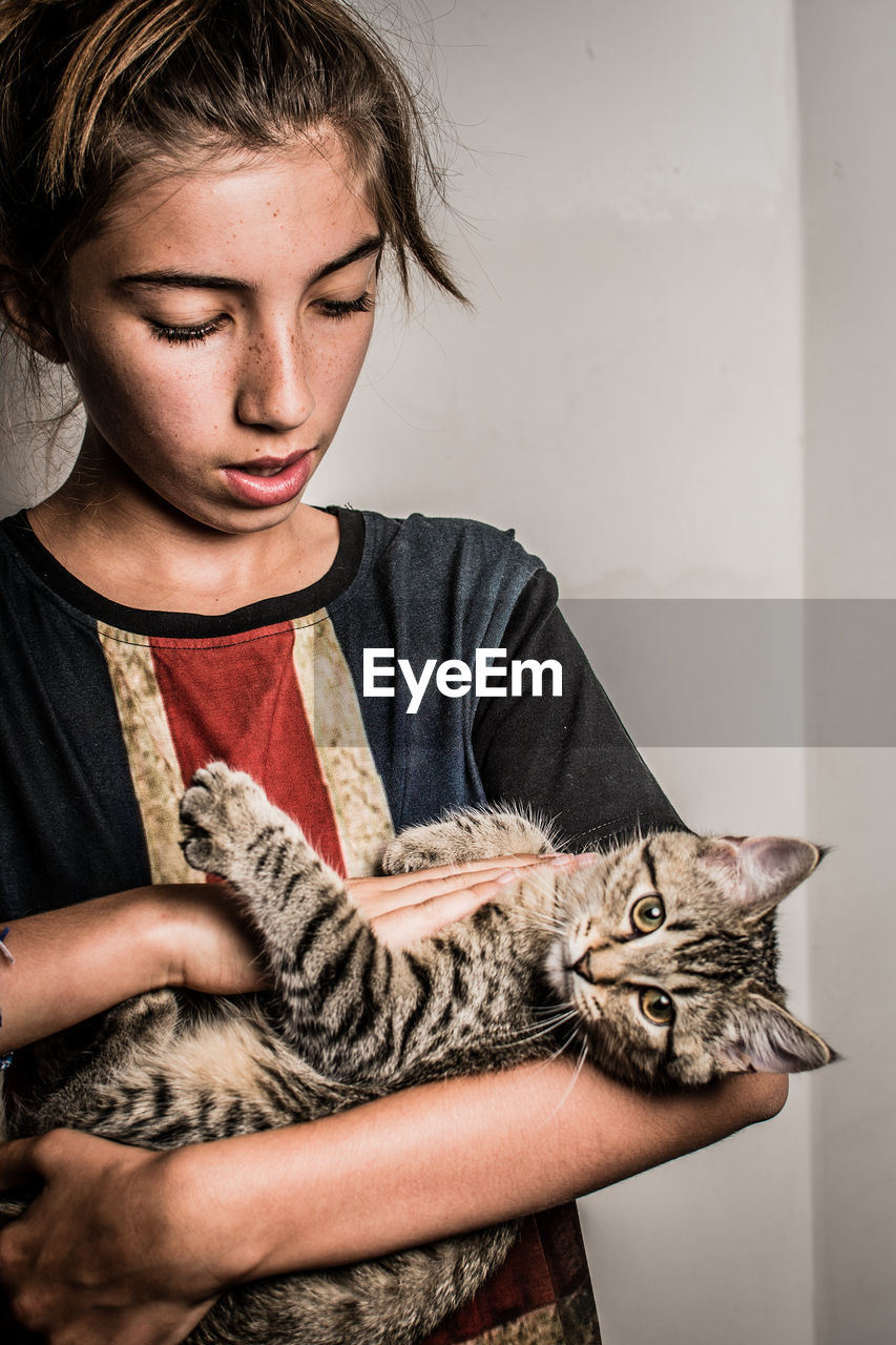 Girl holding cat against wall