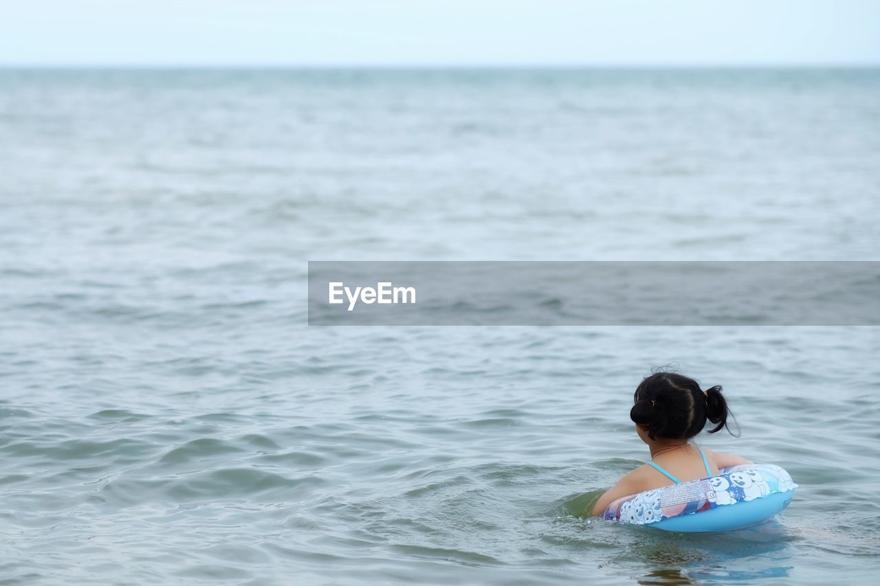 Rear view of girl with inflatable ring swimming in sea