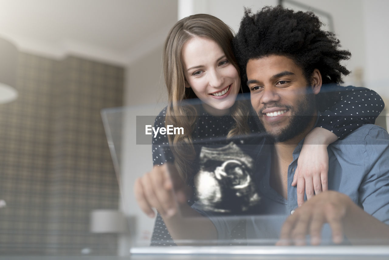 Smiling couple looking at ultra sound picture of baby on futuristic screen