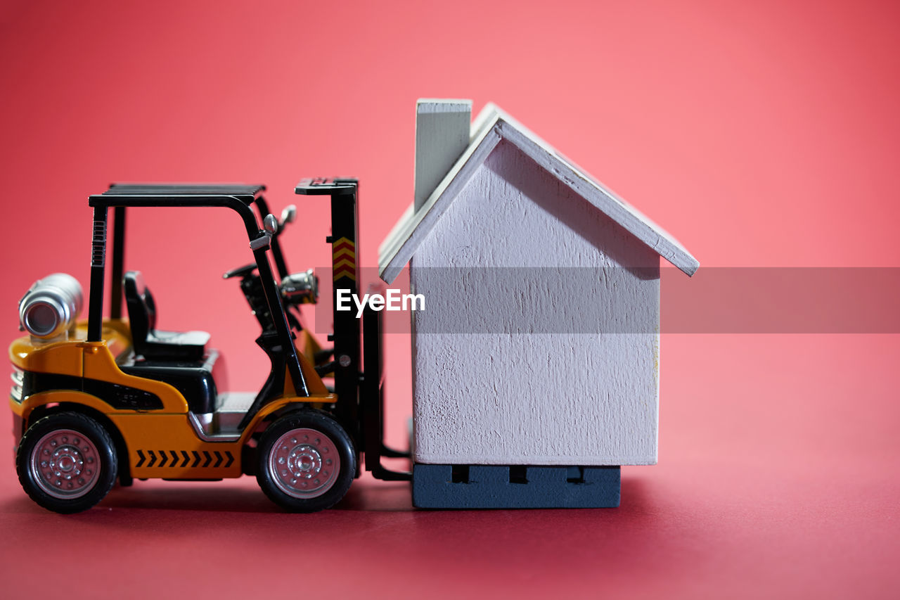 House moving concept with miniature forklift and model house on red background