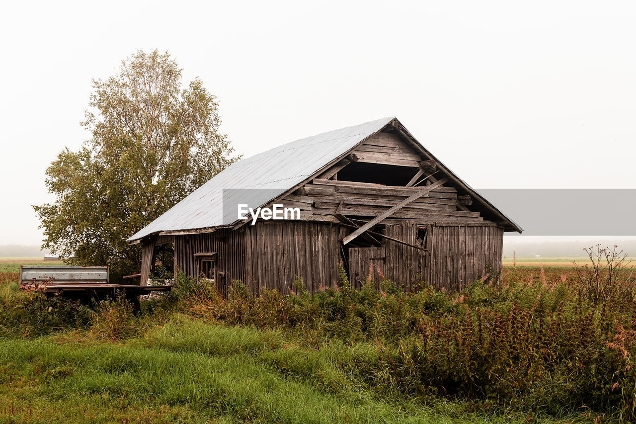 A rusty trailer parked by an old abandoned barn house on the autumn fields of the rural finland. 