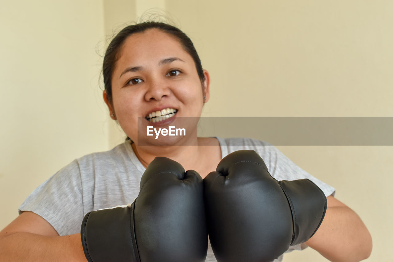 Portrait of smiling young woman against wall with boxing gloves