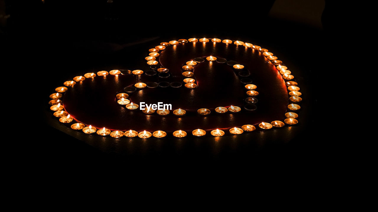 Lit tea light candles arranged in heart shape against black background