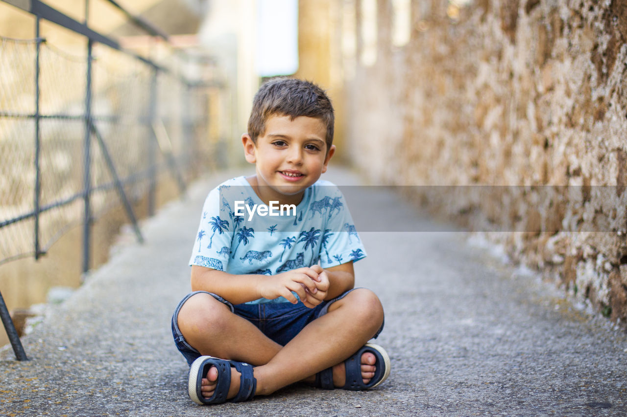 Portrait of smiling boy sitting on footpath