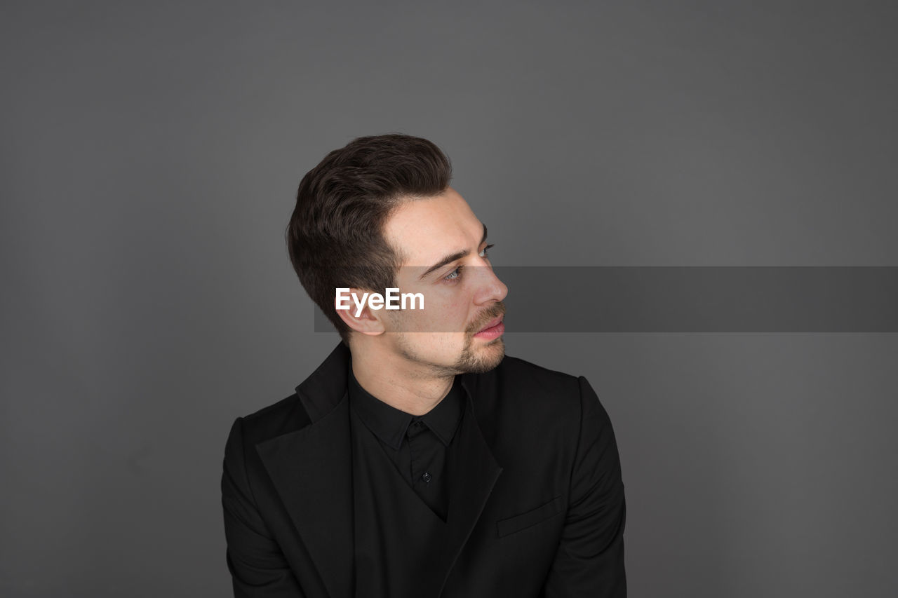 YOUNG MAN LOOKING AWAY AGAINST GRAY BACKGROUND