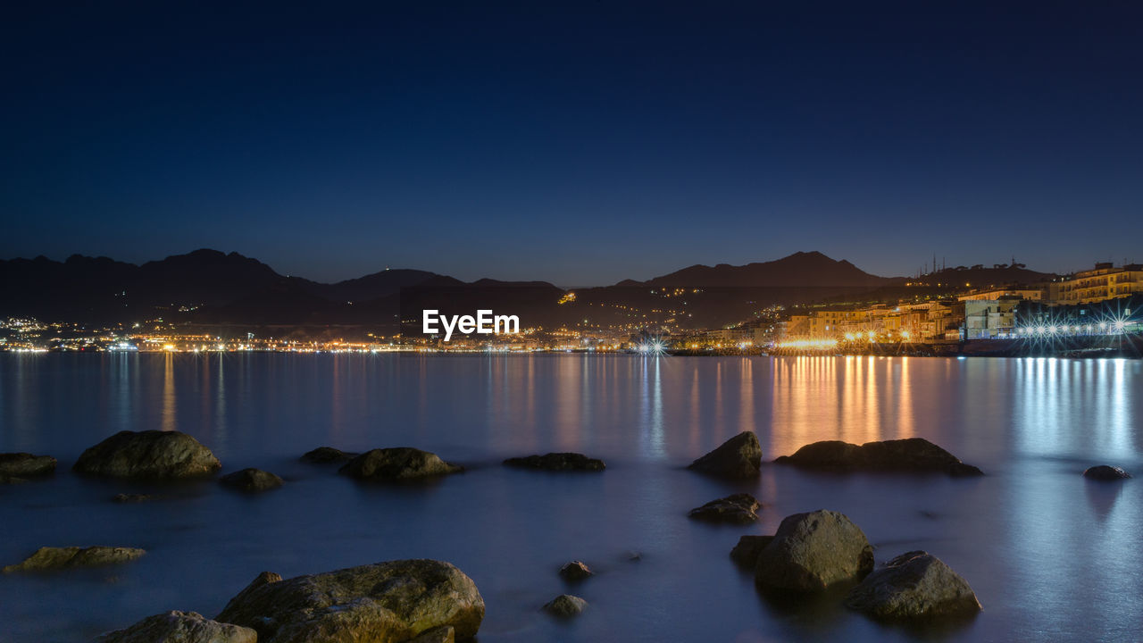 ILLUMINATED ROCKS BY SEA AGAINST CLEAR SKY