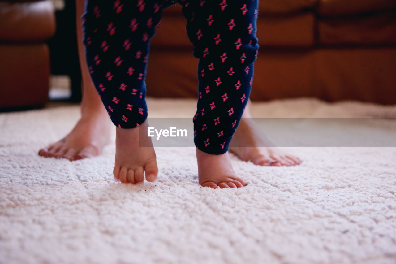 Low section of mother and baby girl walking on rug at home
