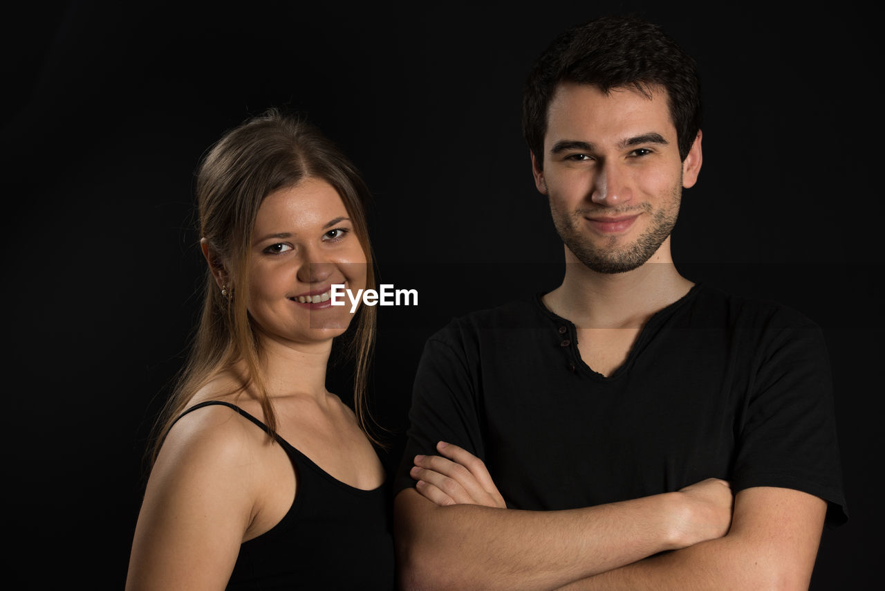 Portrait of smiling young couple against black background