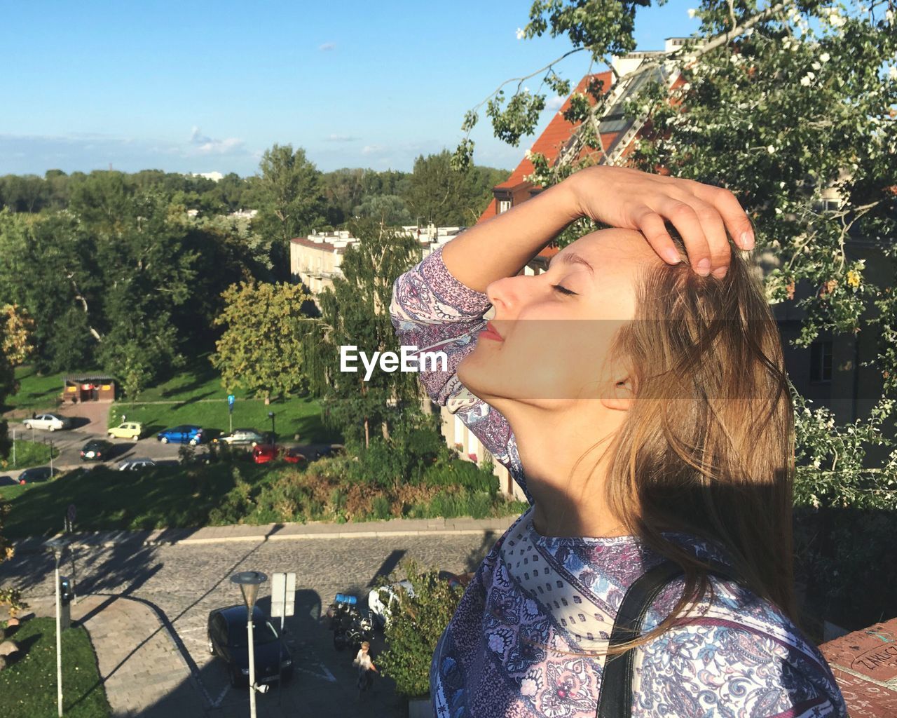 Young woman with eyes closed standing outdoors on sunny day