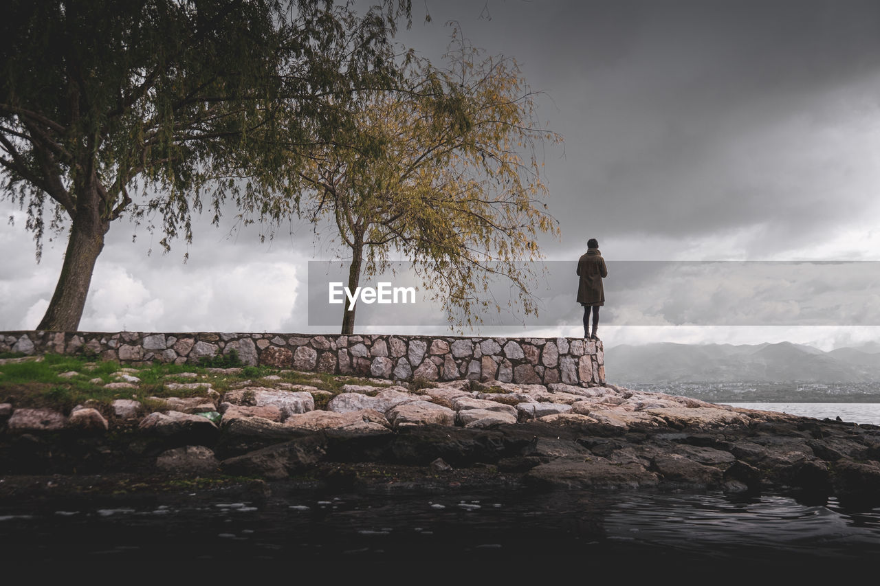 Man standing on rock by sea against sky