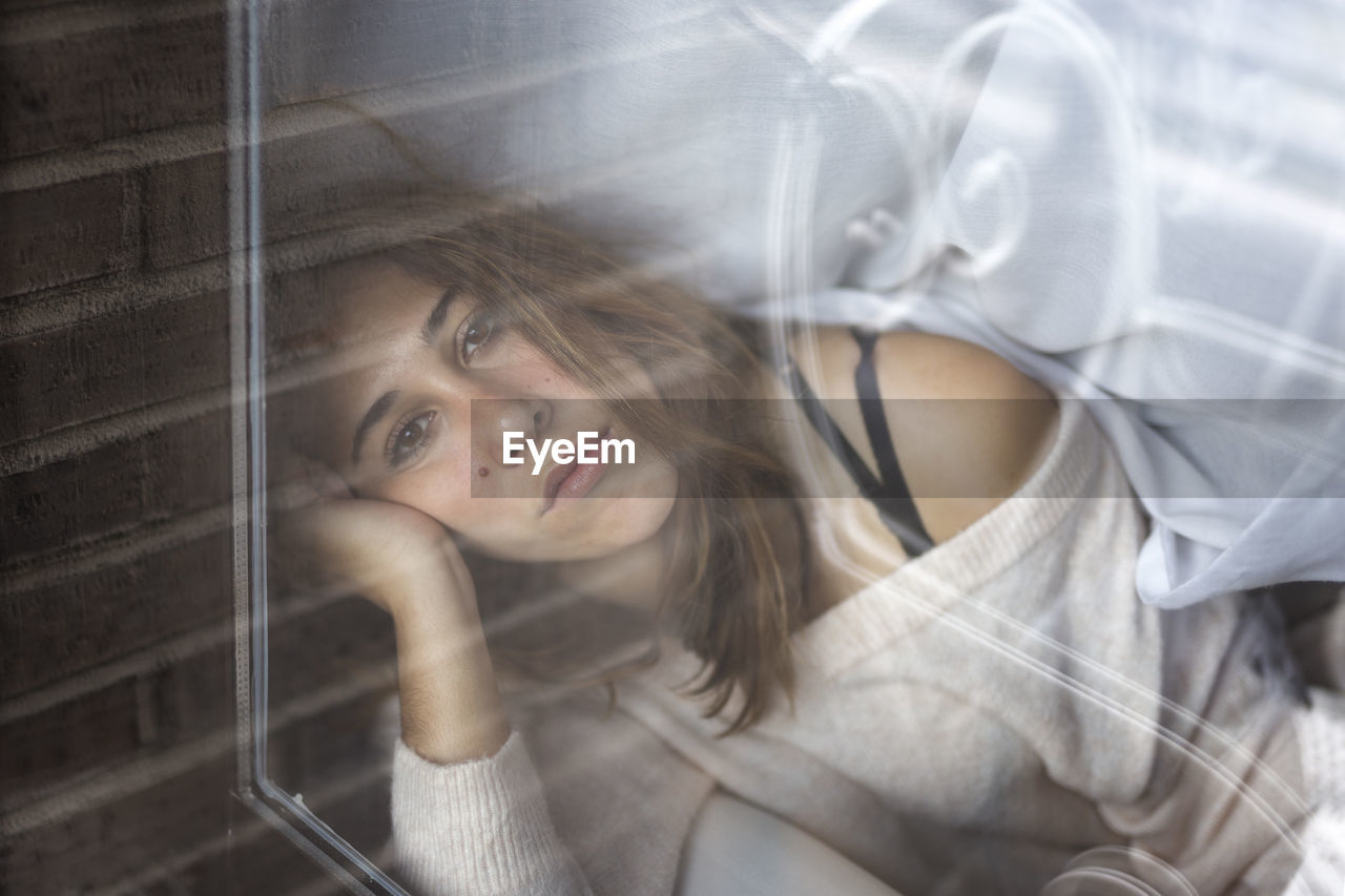 Portrait of beautiful young woman looking through window