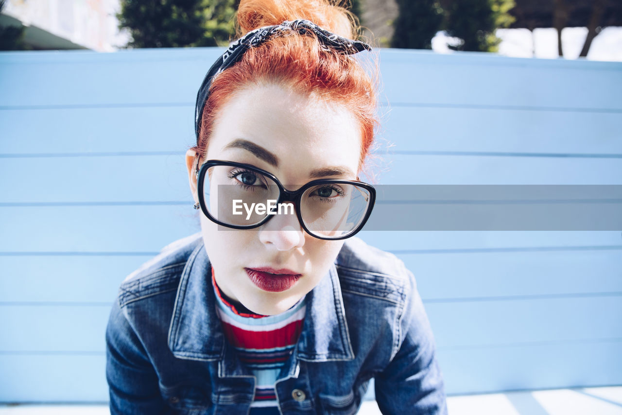 Portrait of redhead young woman wearing eyeglasses while sitting on bench