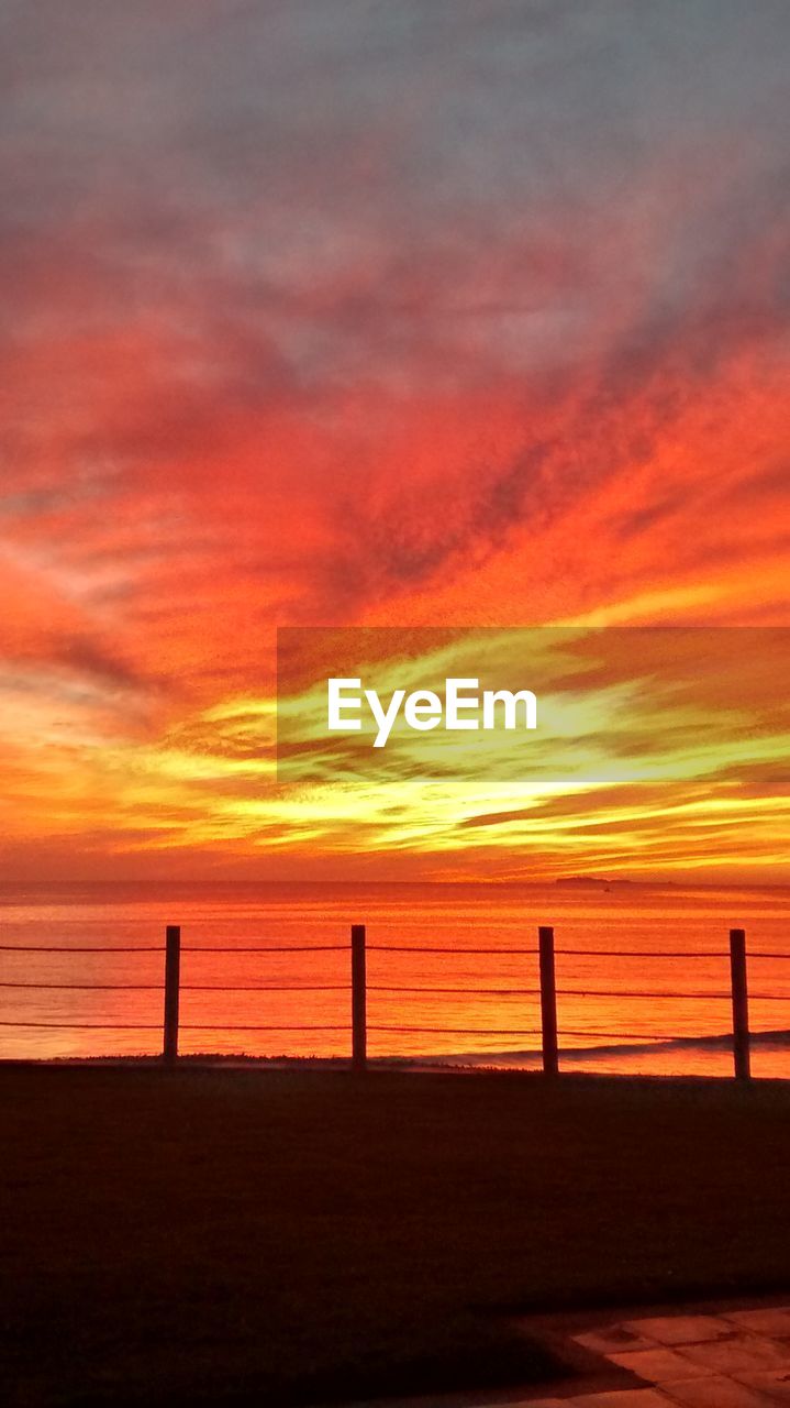 Silhouette railing by sea against dramatic sky at dusk