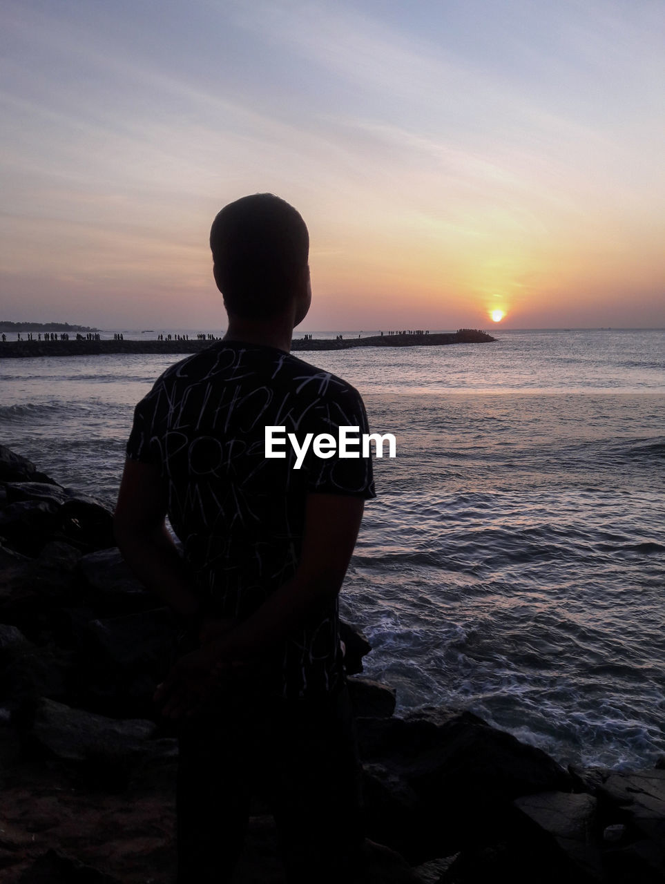 Rear view of man looking at sea against sunset sky