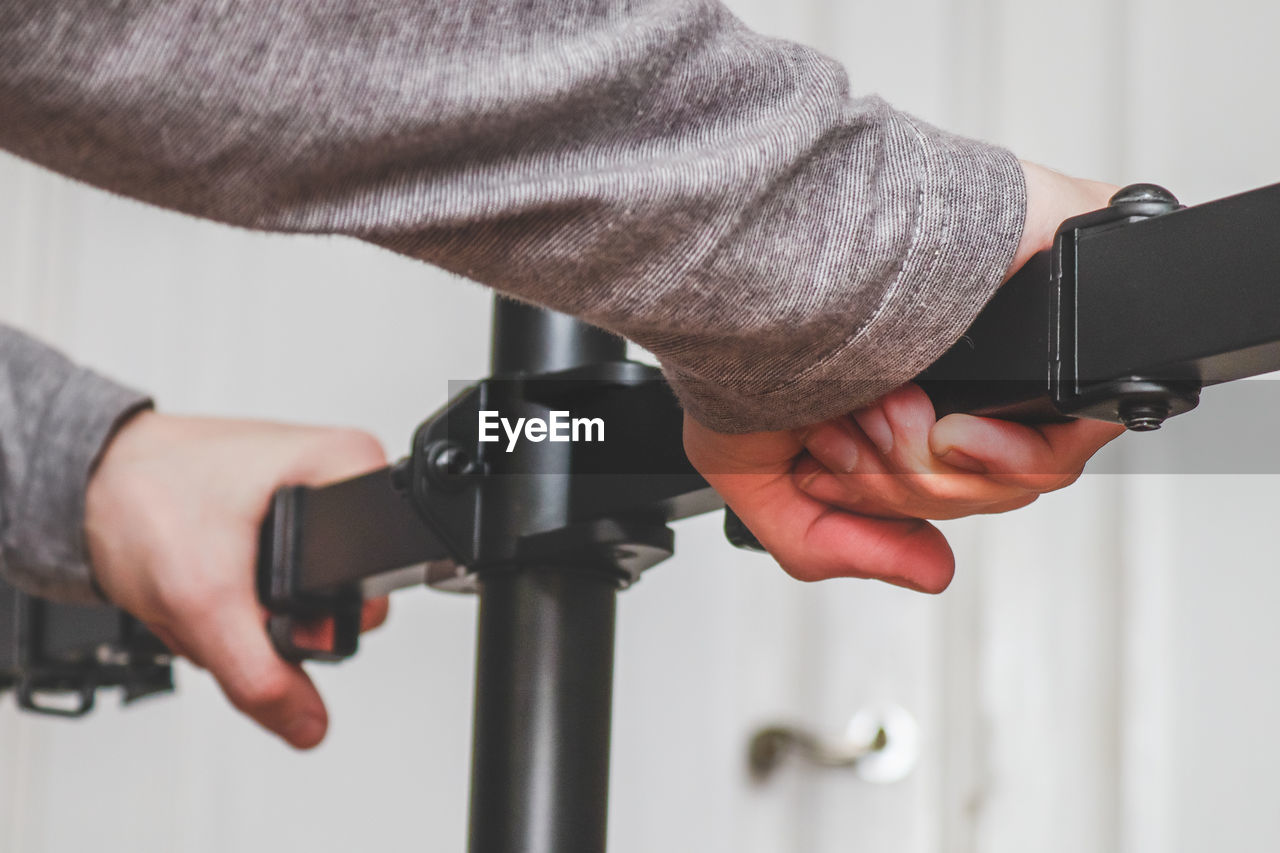 The hands of a young caucasian guy sets up a bracket for a monitor in his room 