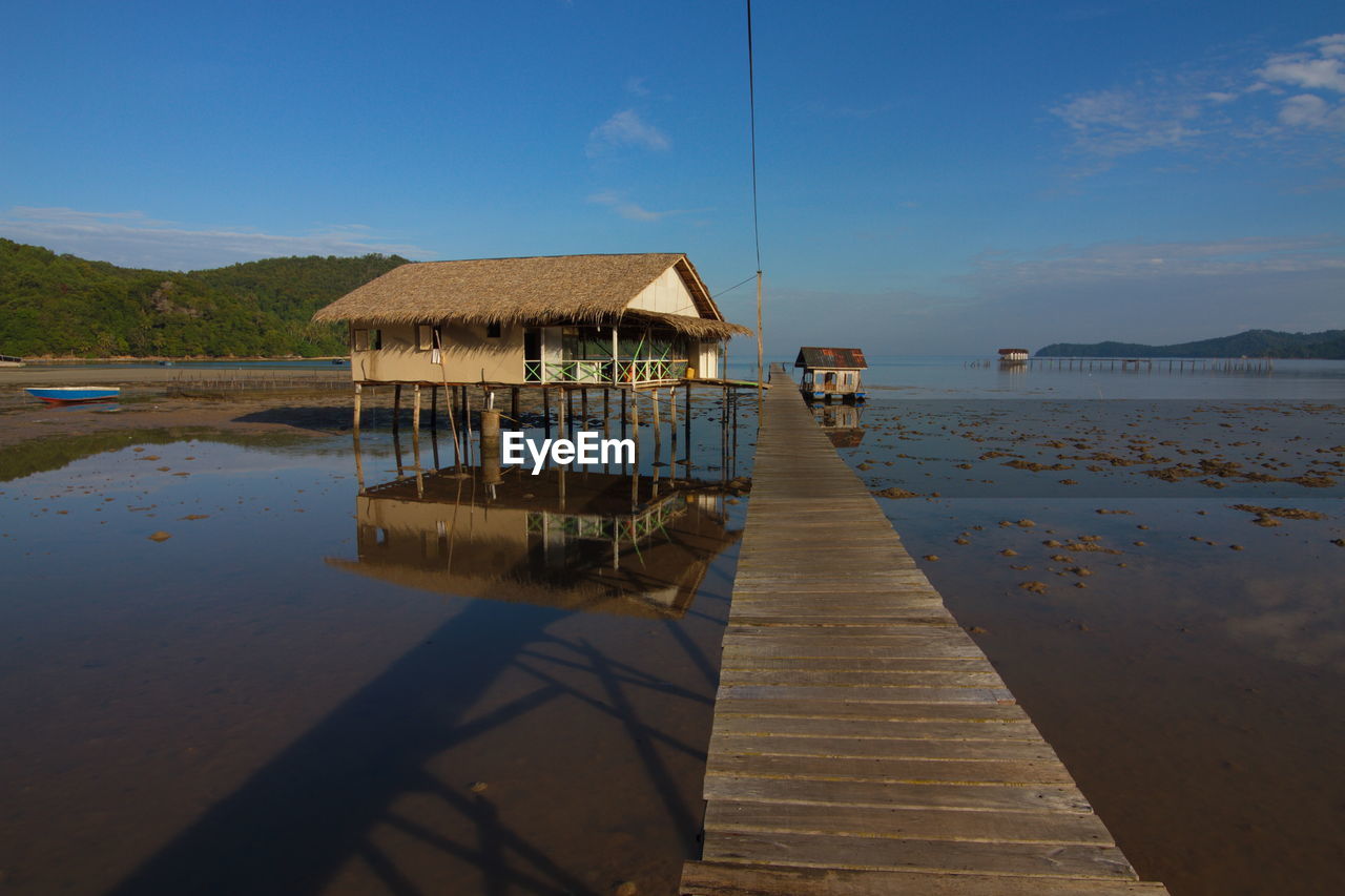 Pier on lake by houses against sky