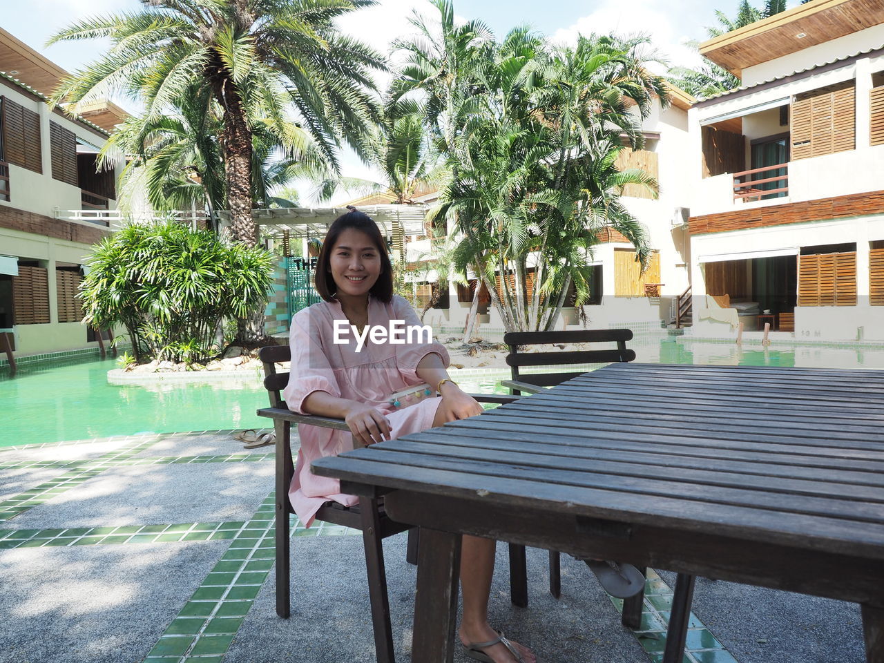 Portrait of young woman sitting in swimming pool against building