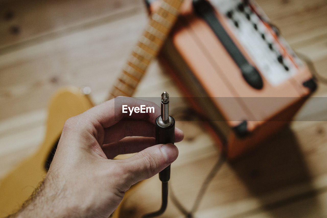 Cropped hand of person holding interconnect plug over guitar and equipment