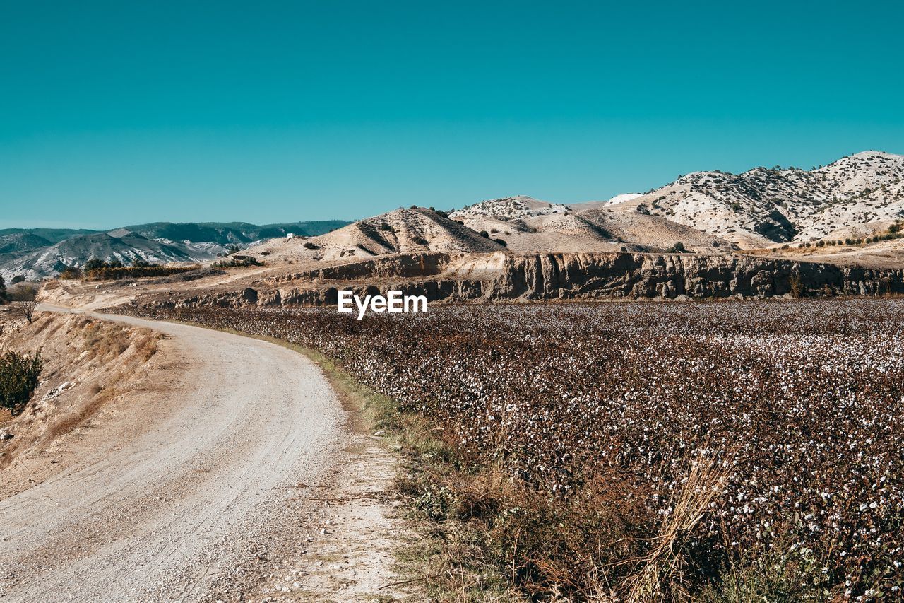 Dirt road on landscape against clear blue sky