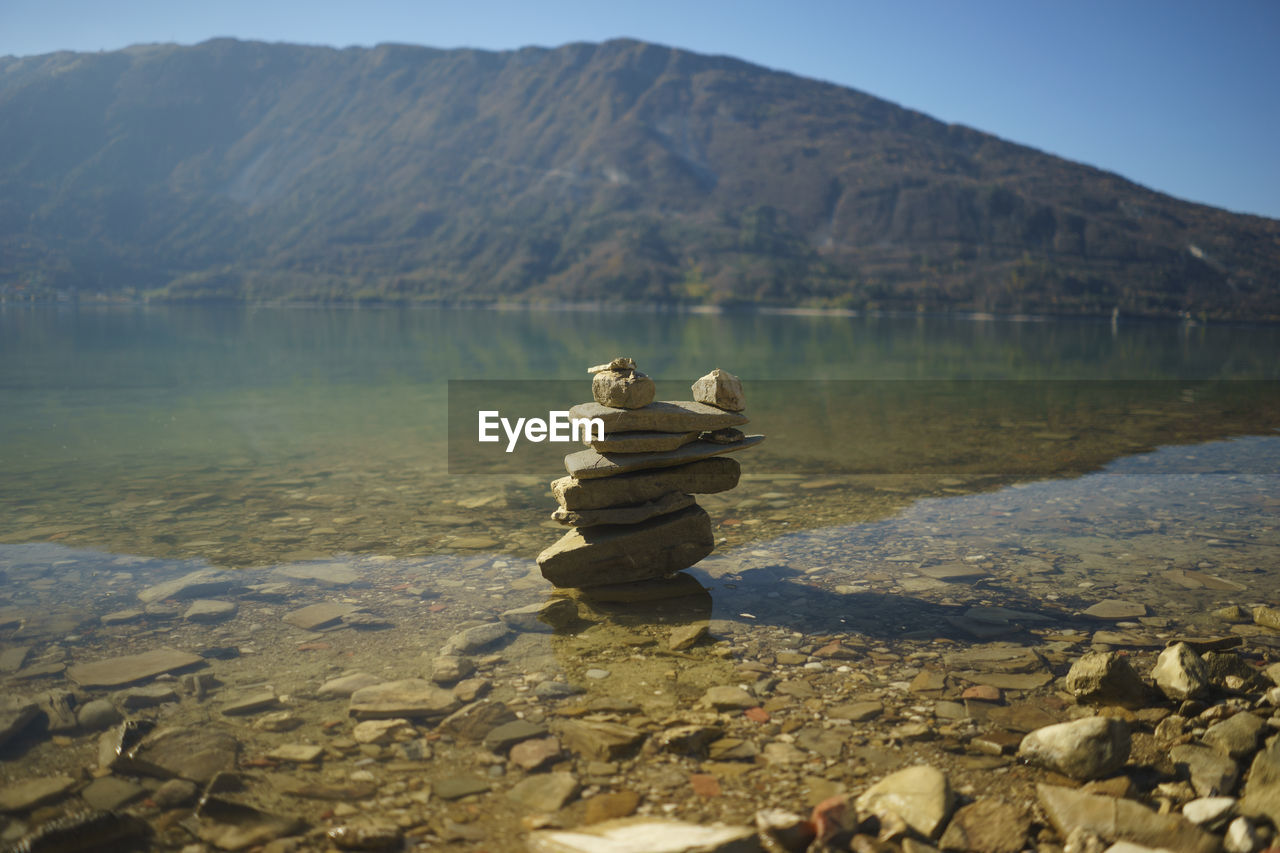 Stack of rocks at lakeshore against mountain