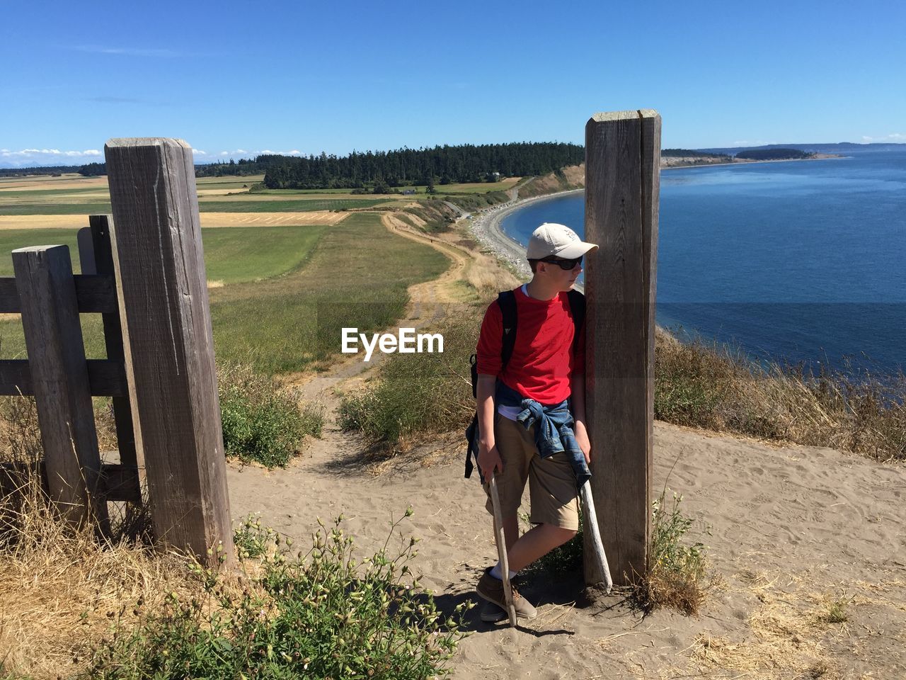 Boy in hat standing on hill against sea and sky during sunny day