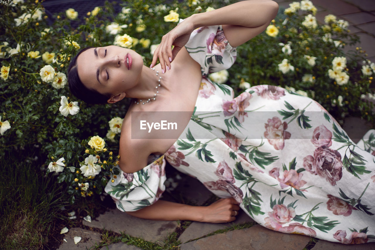 Outdoor portrait of a beautiful girl in a dress lying on the ground next to a white roses