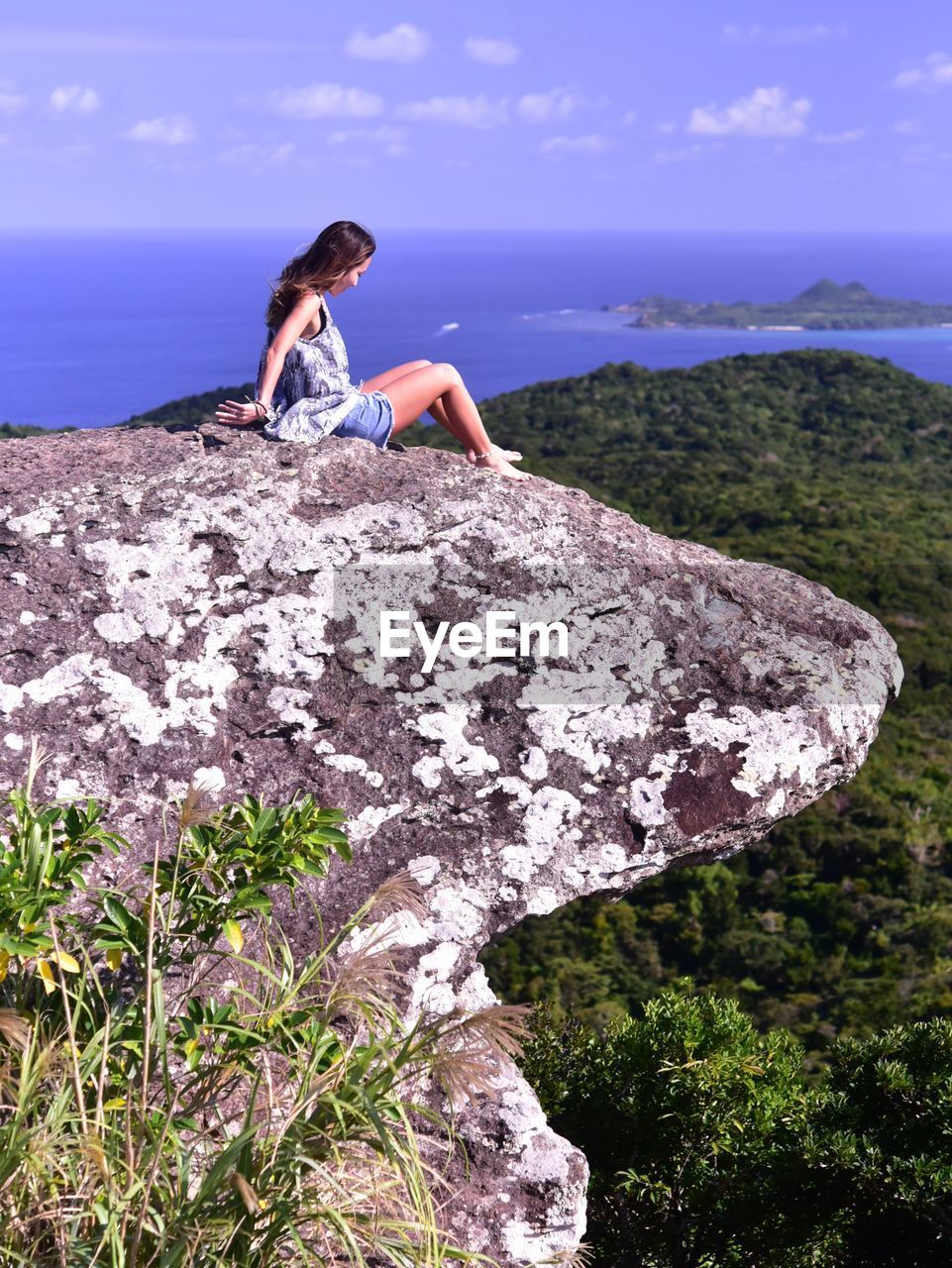 Woman sitting on rock by sea against sky