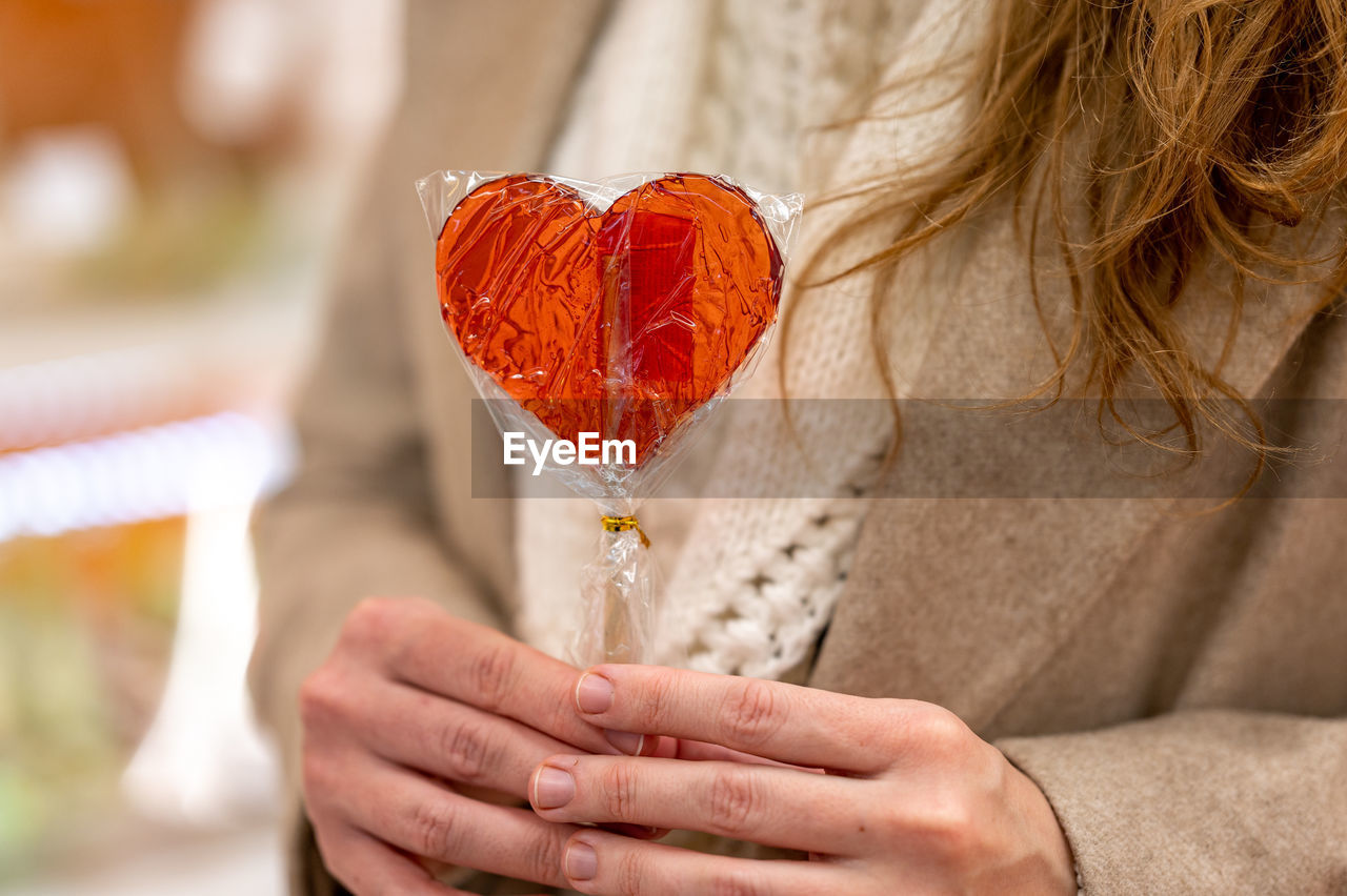 Girl holding a heart-shaped lollipop in her hands. the girl's face is not visible. valentine's day