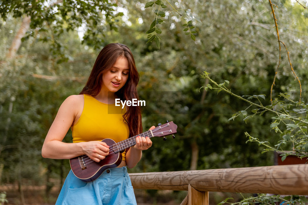 Young woman holding guitar against trees
