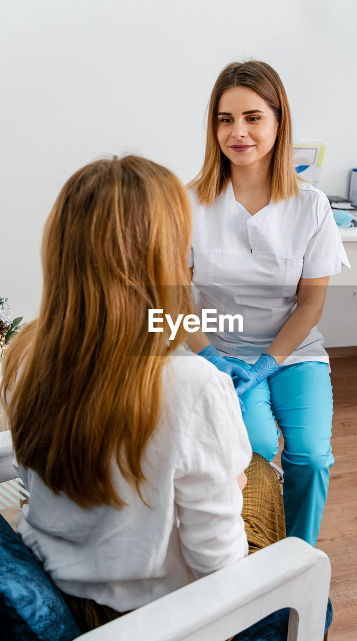 Female professional beauty doctor talking with pretty young female.