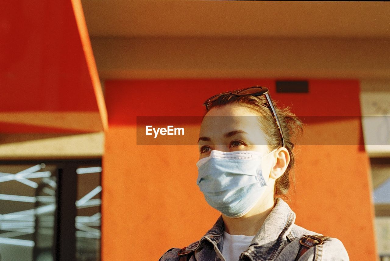 Close-up of woman wearing mask standing against building