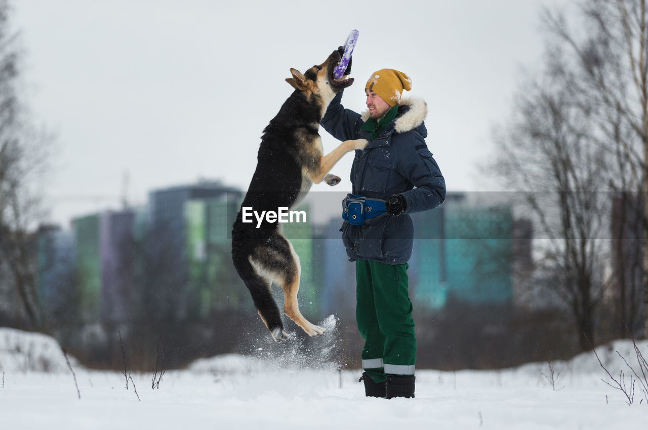 Man and dog playing with plastic ring during winter