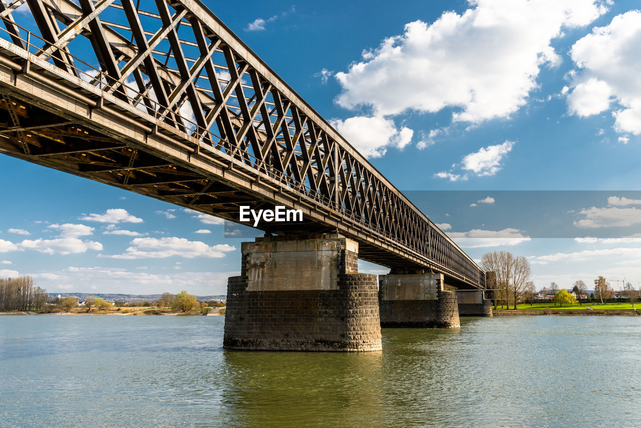 Steel, lattice structure of a railway bridge over a river with a background of blue sky with  clouds
