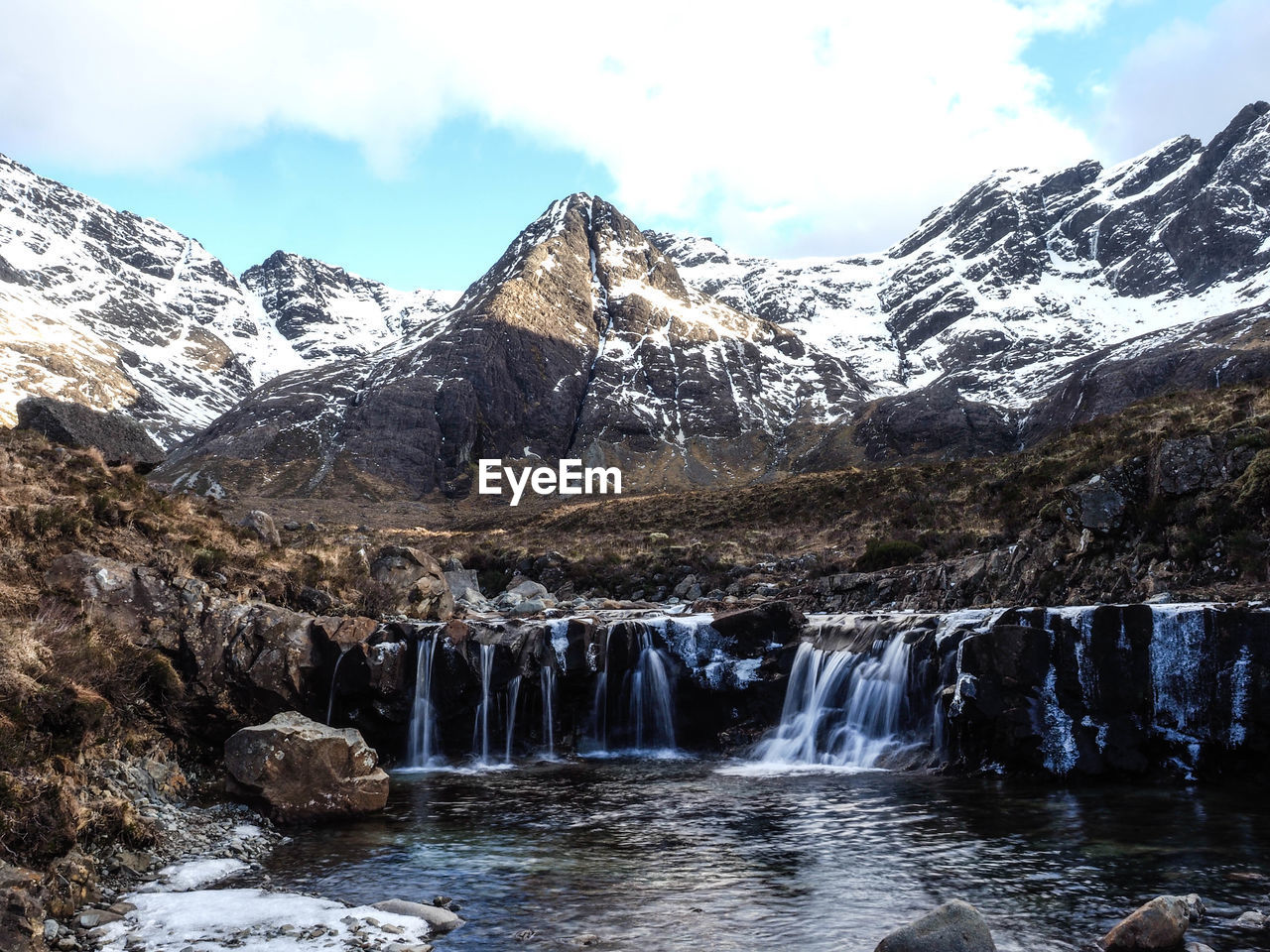 SCENIC VIEW OF WATERFALL AGAINST SNOWCAPPED MOUNTAINS