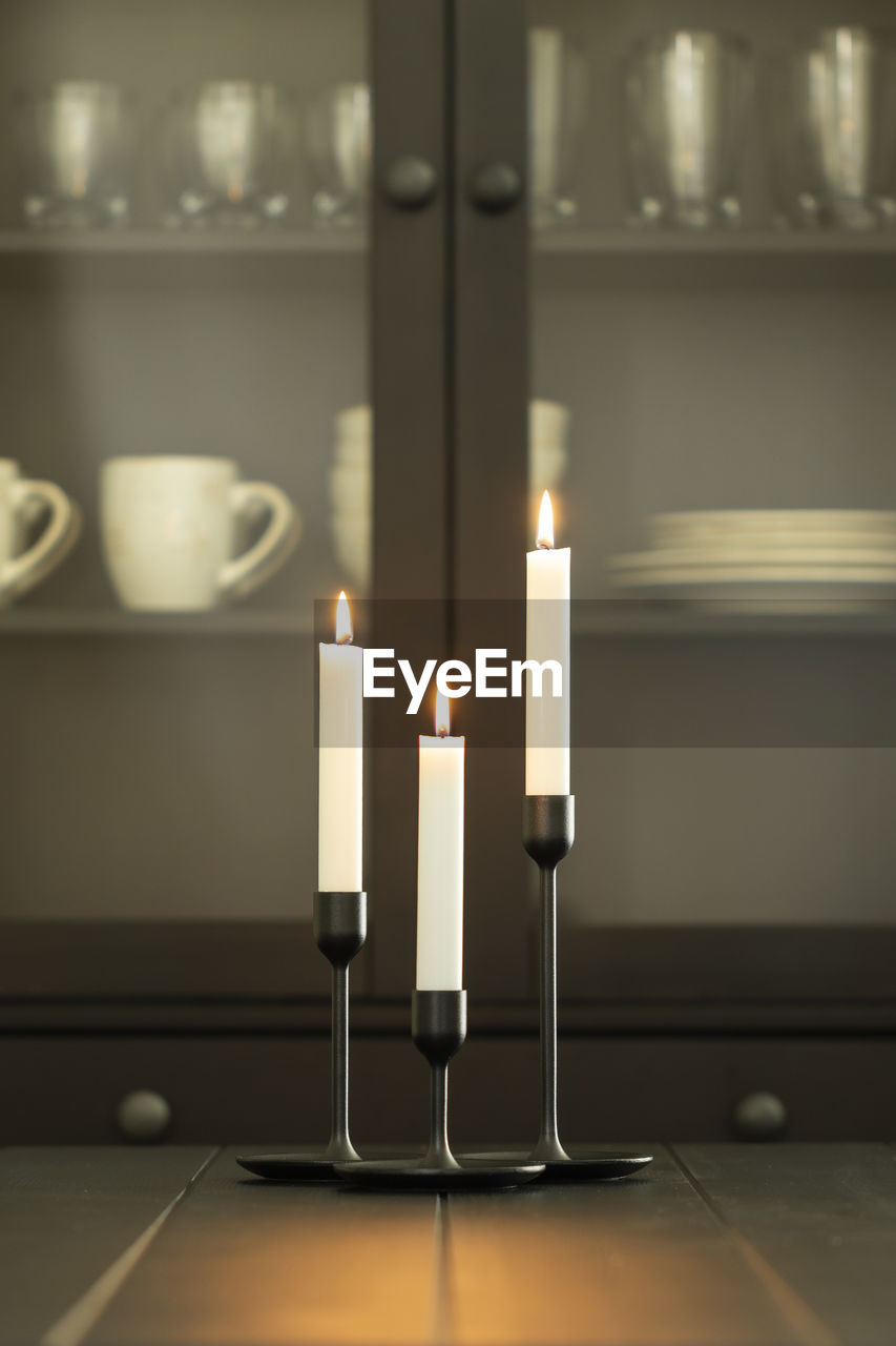 Tree burning white candles in holders over black dining table - vertical