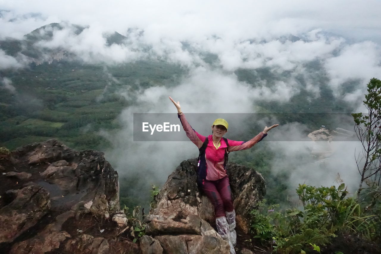 High angle view of female hiker sitting on rock with arms outstretched at mountain peak