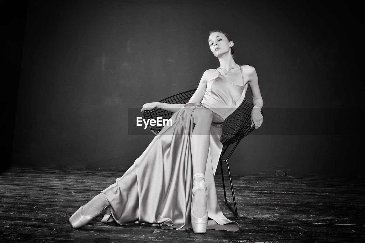 Portrait of a ballerina in a pink dress is sitting on a chair with her leg in the slit of the dress