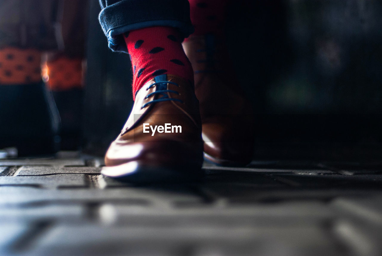 Low section of man wearing shoes while walking on cobblestone