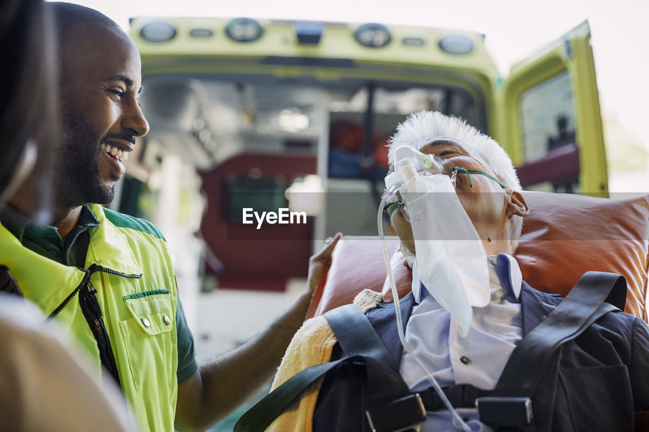 Smiling male paramedic encouraging businessman against ambulance