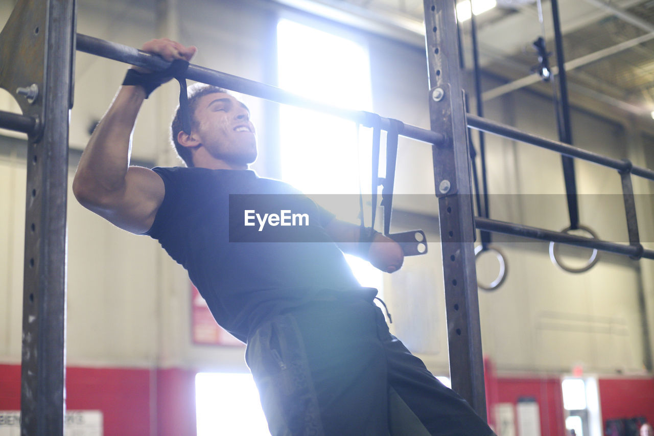 Confident male adaptive athlete screaming while doing chin-ups in gym