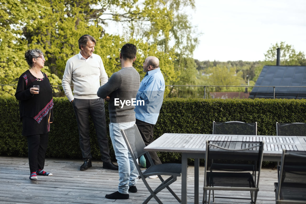 Multi-ethnic friends talking while standing by table in yard