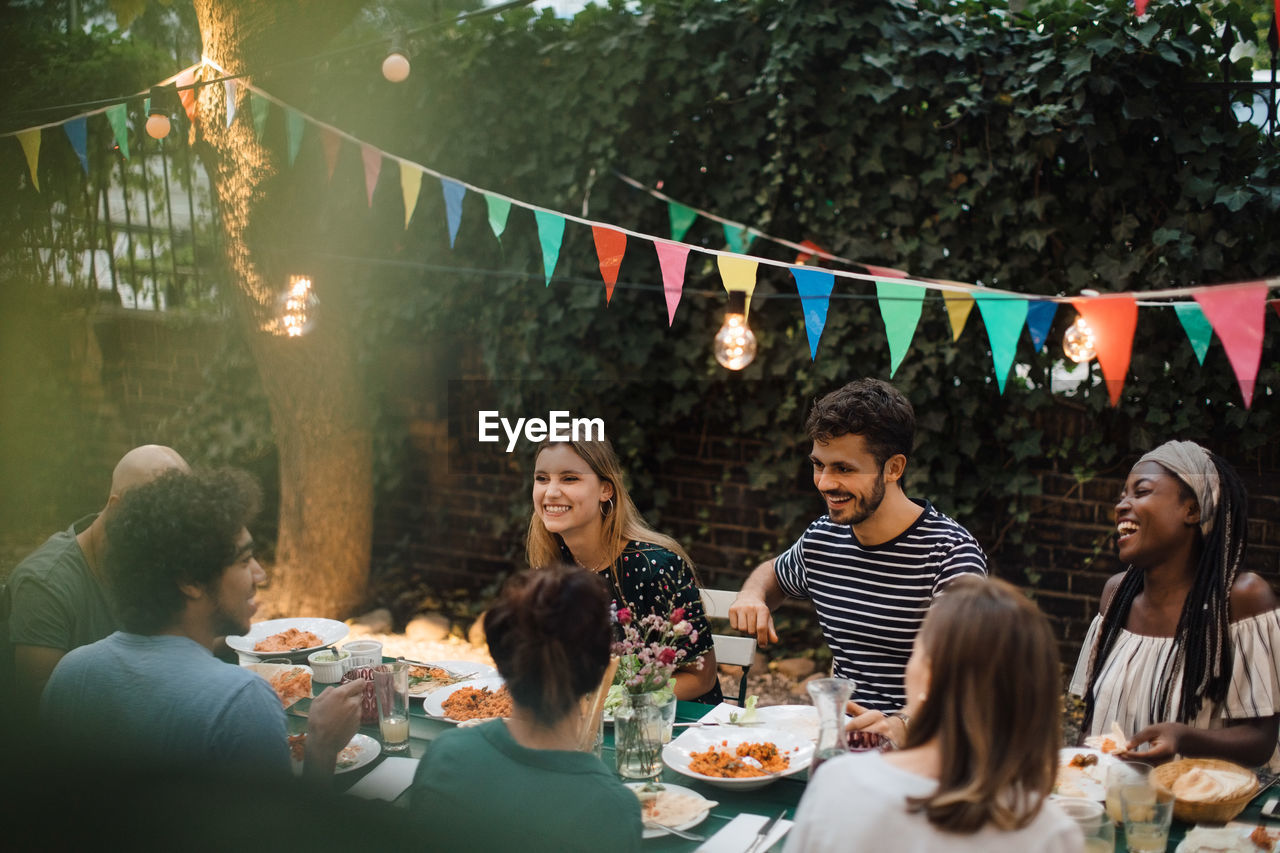 Multi-ethnic young friends enjoying dinner at table during garden party