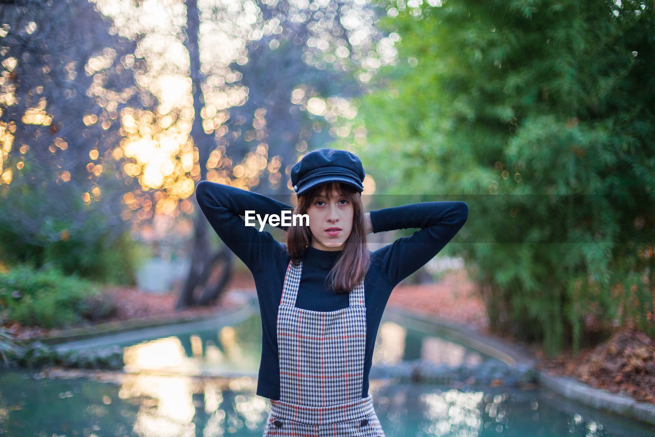 Portrait of young woman standing by swimming pool against trees