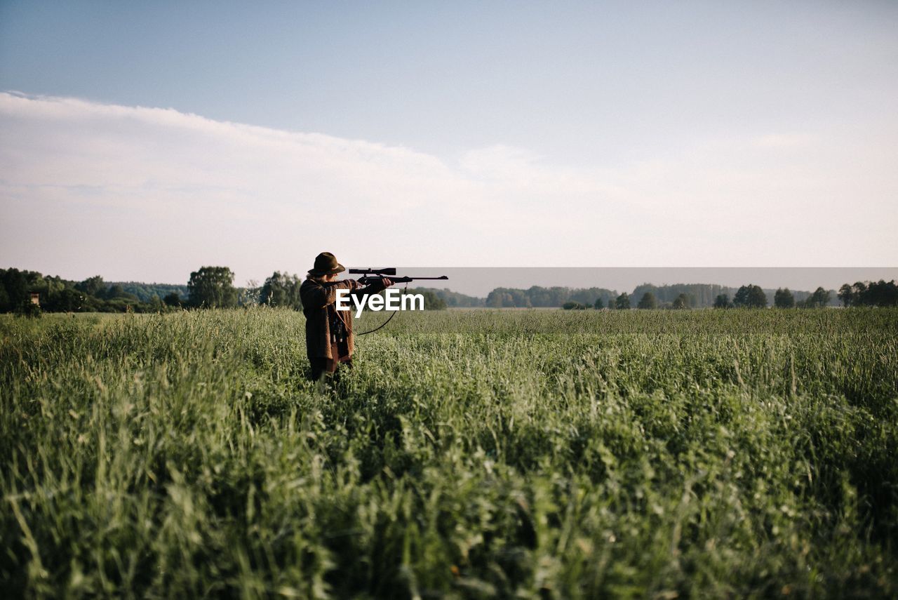 Person aiming with gun amidst grass on field