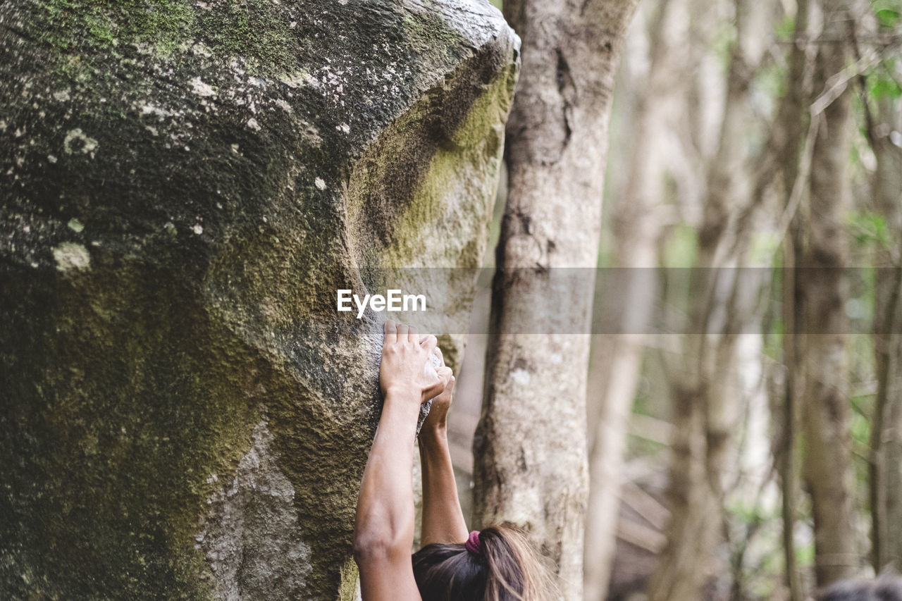 Upper body of a female climber climbing a rock in a forest