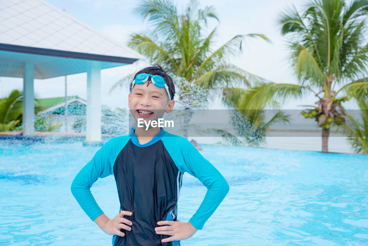 Smiling boy with hands on hip posing in swimming pool