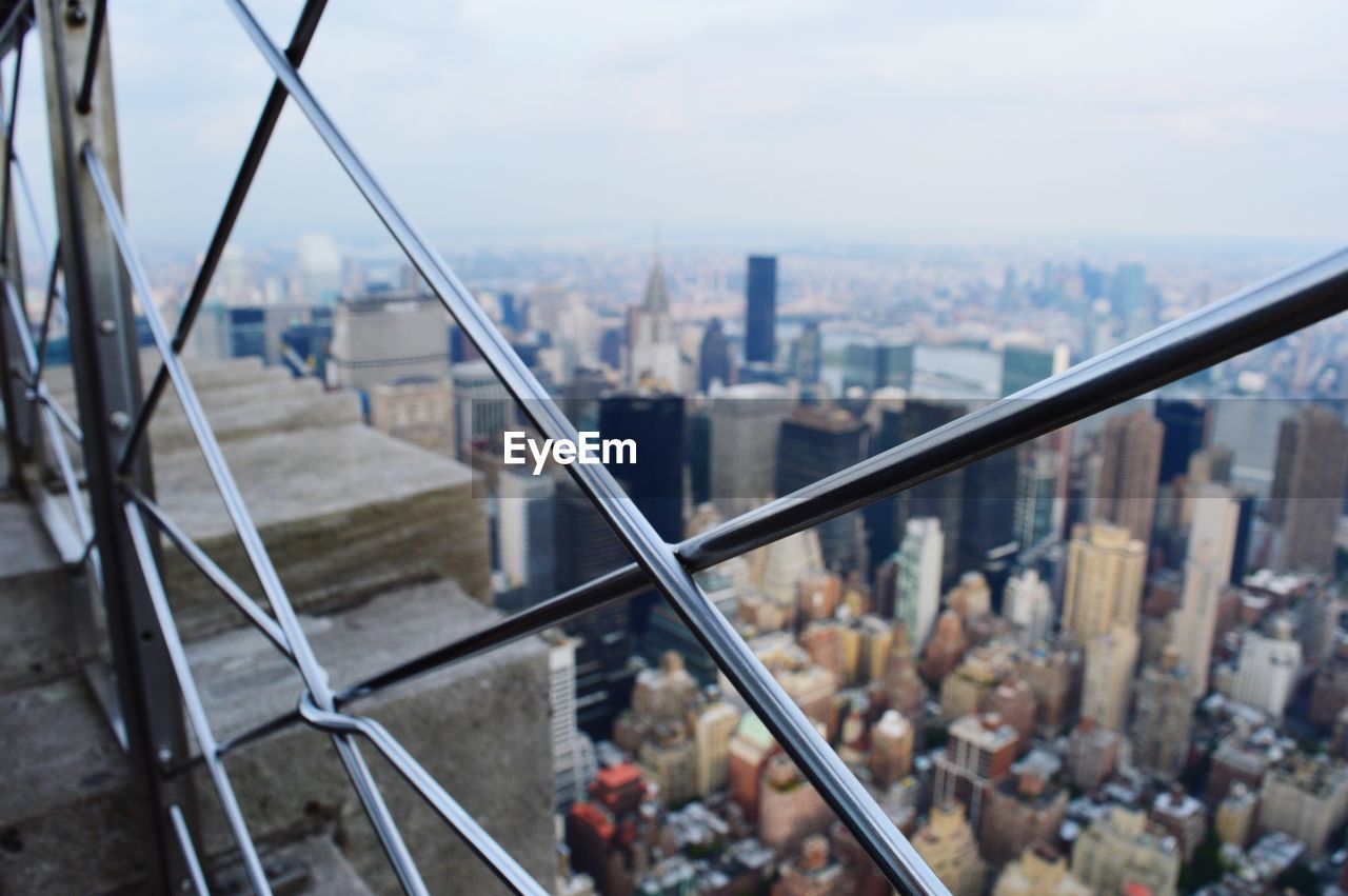 High angle view of buildings against sky seen through chainlink fence