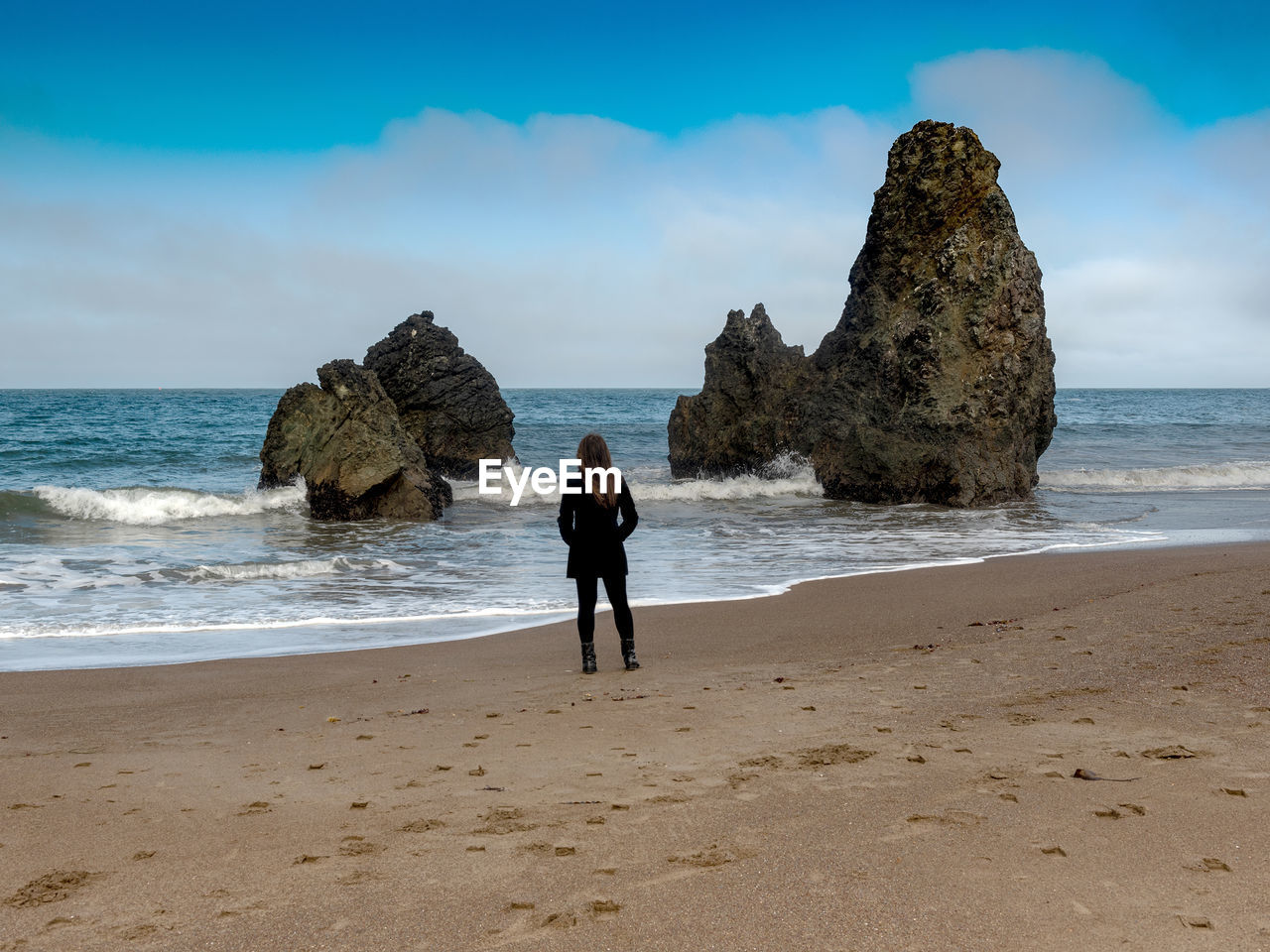 REAR VIEW OF FRIENDS ON ROCKS AT BEACH AGAINST SKY