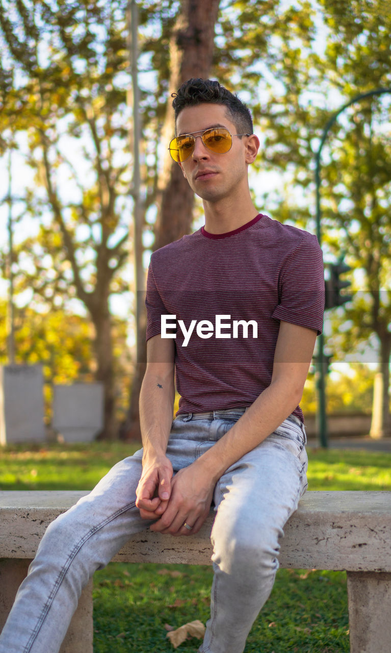 Portrait of young man wearing sunglasses while sitting on bench at park